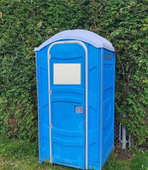Portable toilet next to a hedge at a ball field